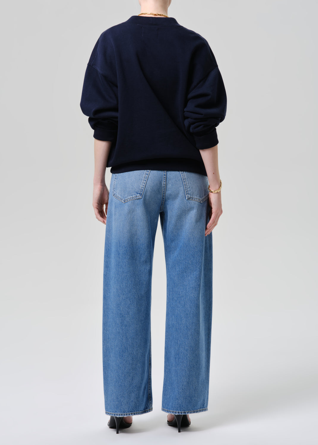 Person wearing a navy sweater and light blue jeans on a grey background
