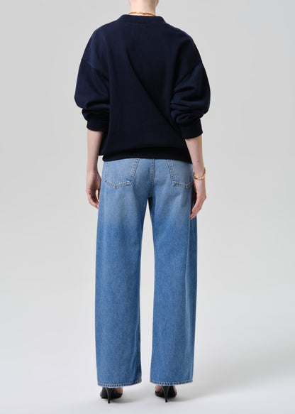 Person wearing a navy sweater and light blue jeans on a grey background