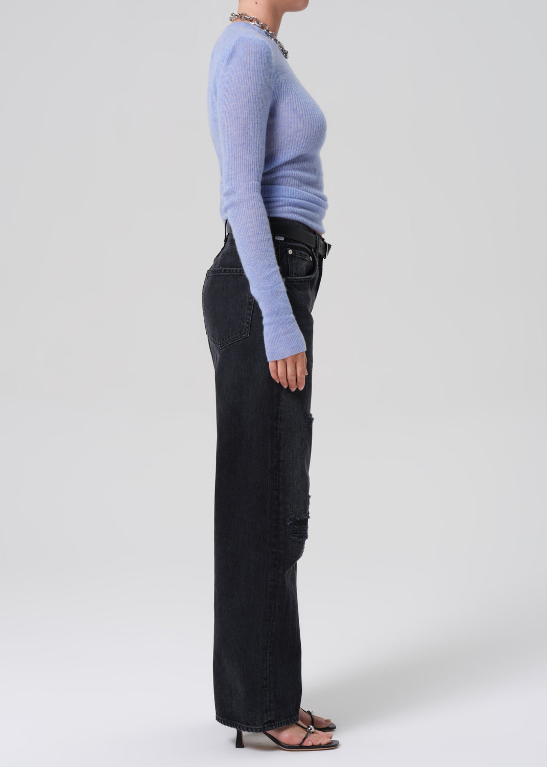 Person wearing a light blue sweater and black pants on a white background