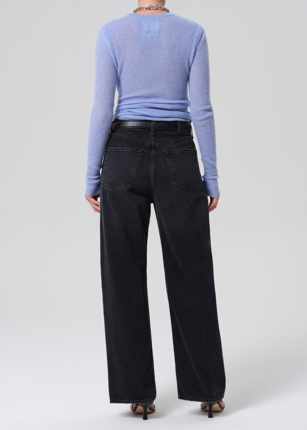 Person wearing a blue sweater and black pants on a white background
