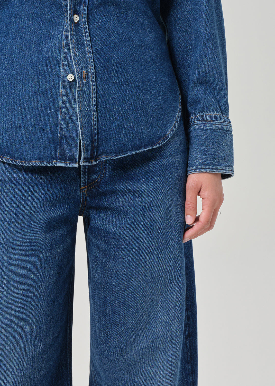 Person wearing a blue denim shirt and jeans on a light gray background