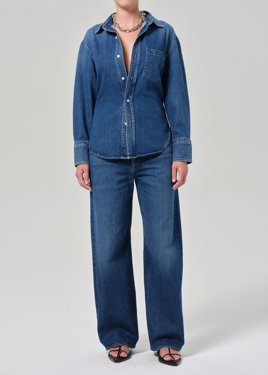 Person wearing a blue denim shirt and jeans on a plain background