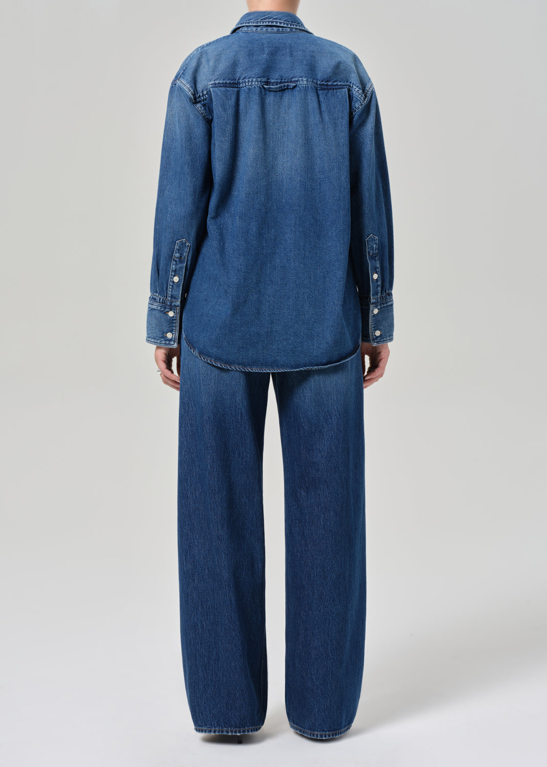 Person wearing a blue denim jacket and pants on a light gray background