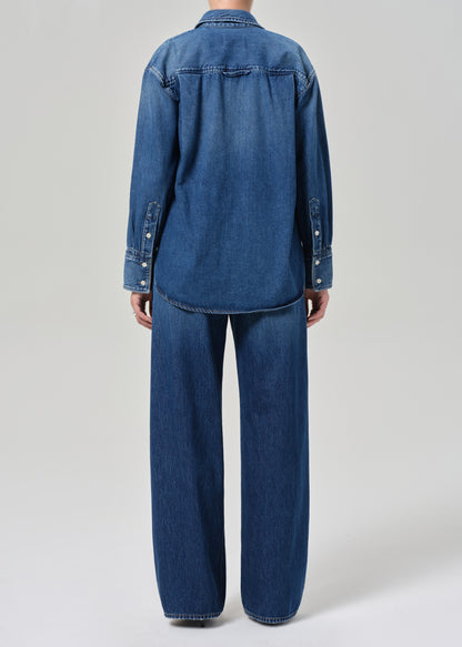 Person wearing a blue denim jacket and pants on a light gray background