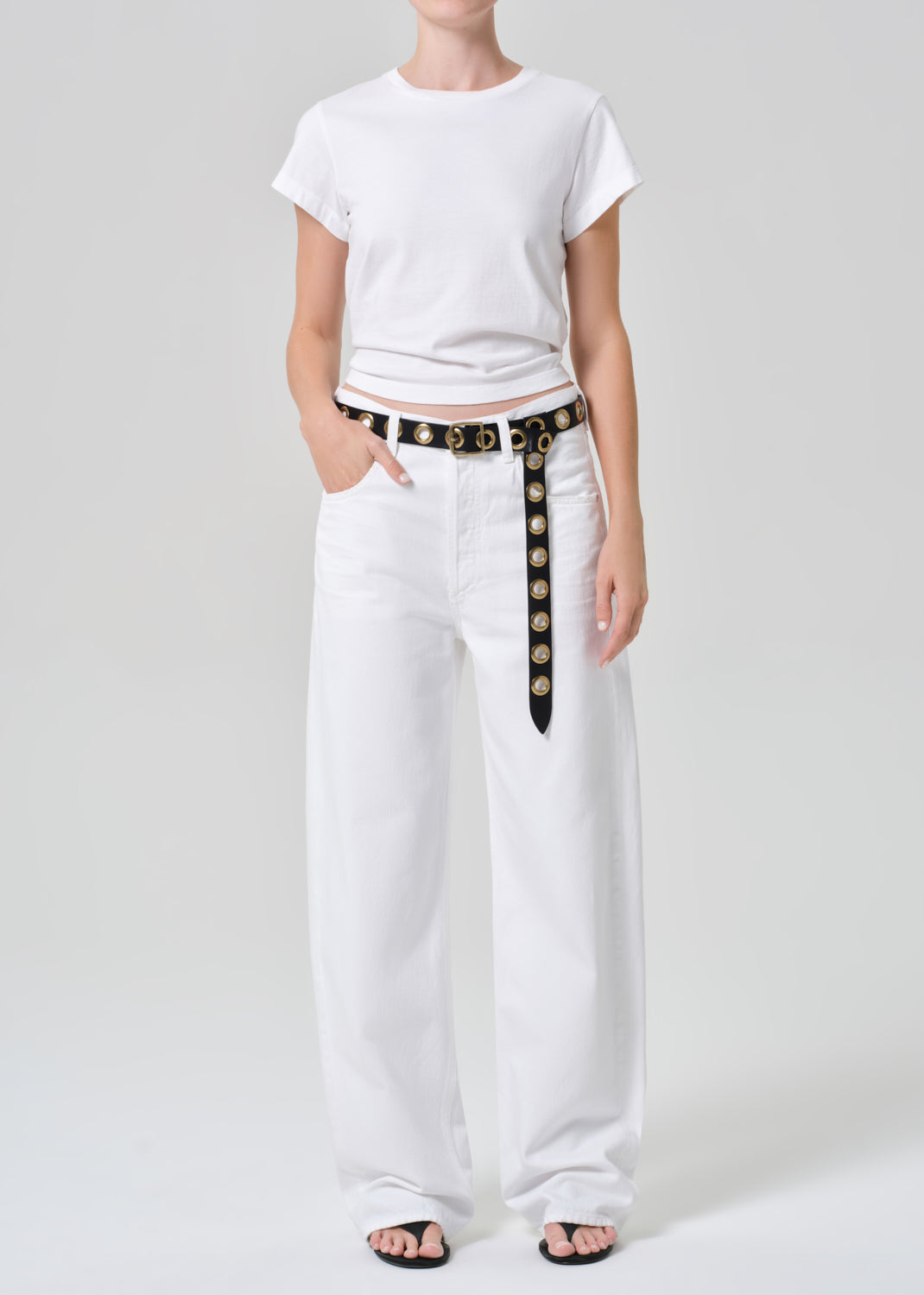 Person wearing a white t-shirt and wide-leg pants with a belt on a plain background