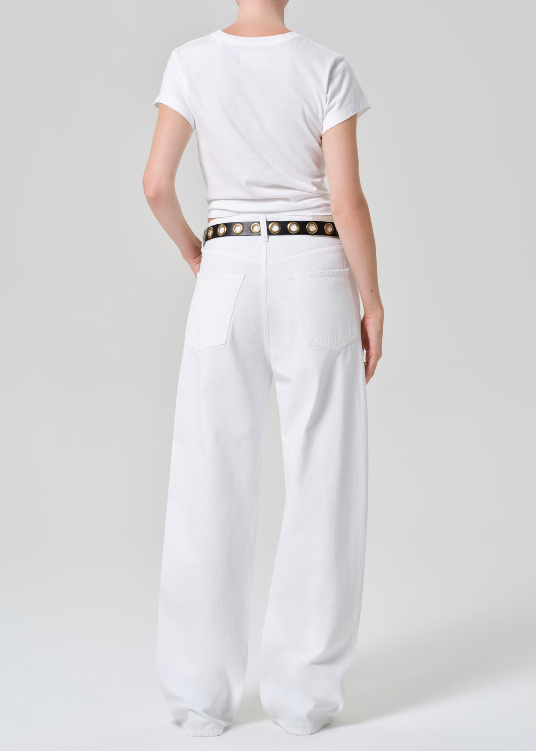 Person wearing a white t-shirt and wide-leg pants with a belt on a plain background