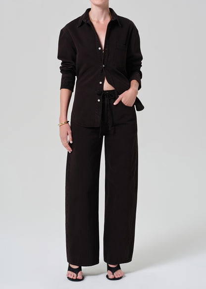 Person wearing a brown button-up shirt with matching wide leg pants outfit on a grey background