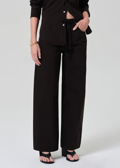 Person wearing a brown button-up shirt with matching wide leg pants outfit on a grey background