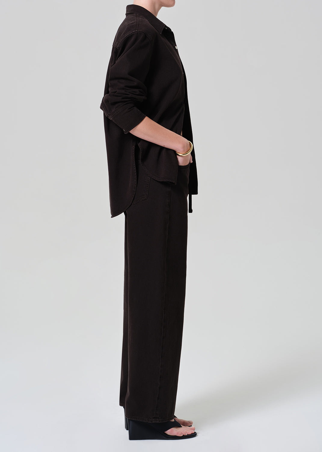 Person wearing a brown button-up shirt with matching wide leg pants outfit on a grey background