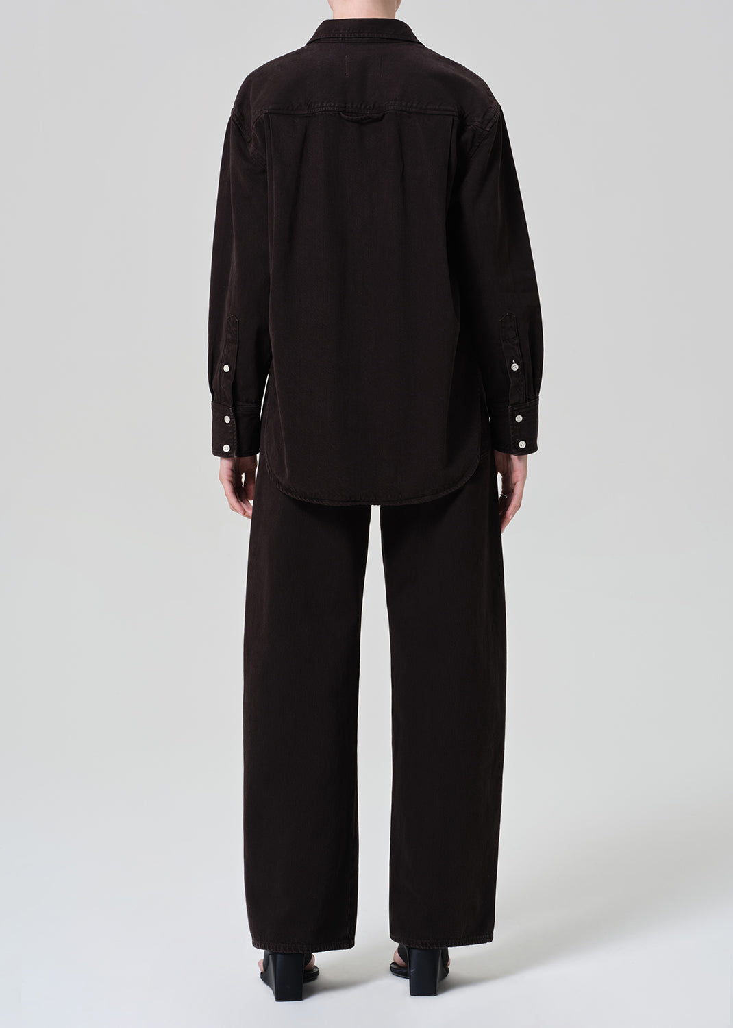 Person wearing a brown button-up shirt with matching wide leg pants outfit on a grey background