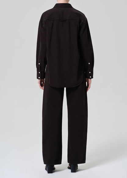 Person wearing a brown button-up shirt with matching wide leg pants outfit on a grey background