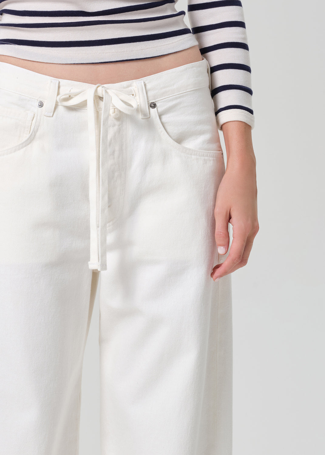 Person wearing a striped shirt and white pants on a plain background