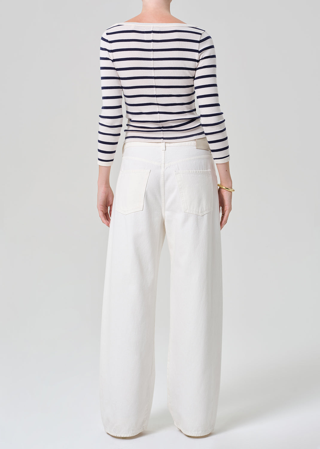 Person wearing a navy and white striped long-sleeve top and white wide-leg pants on a plain background