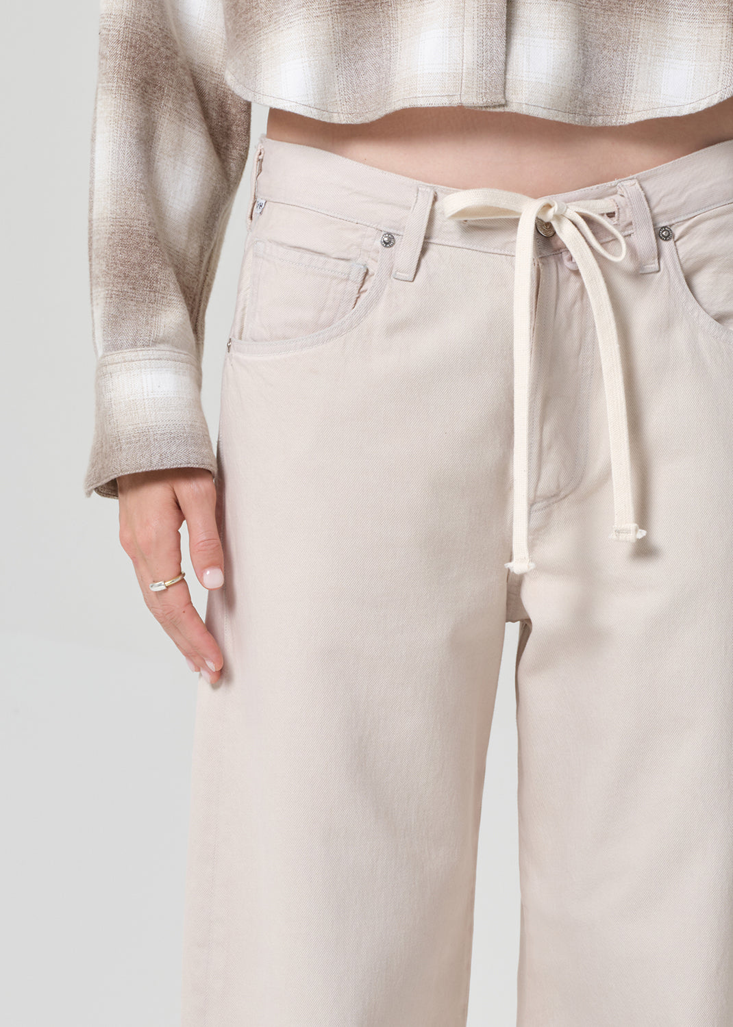 Person wearing a plaid shirt and beige pants on a grey background