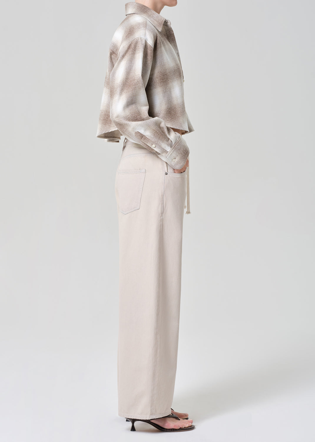 Person wearing a plaid shirt and beige pants on a grey background