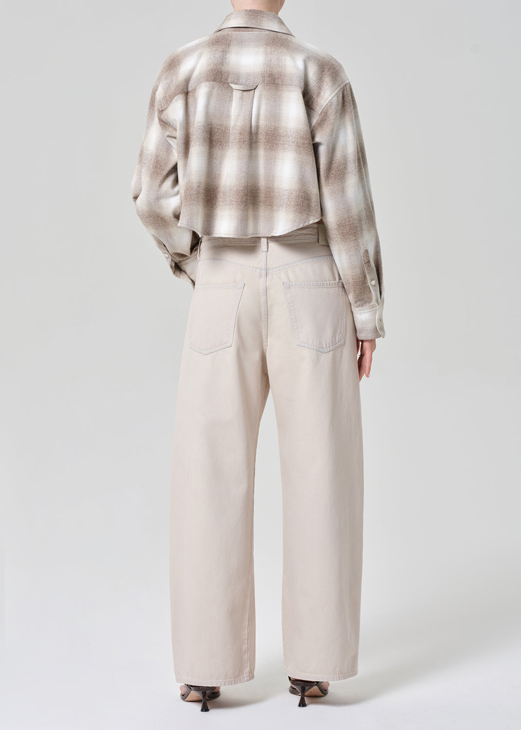 Person wearing a plaid shirt and beige pants on a grey background
