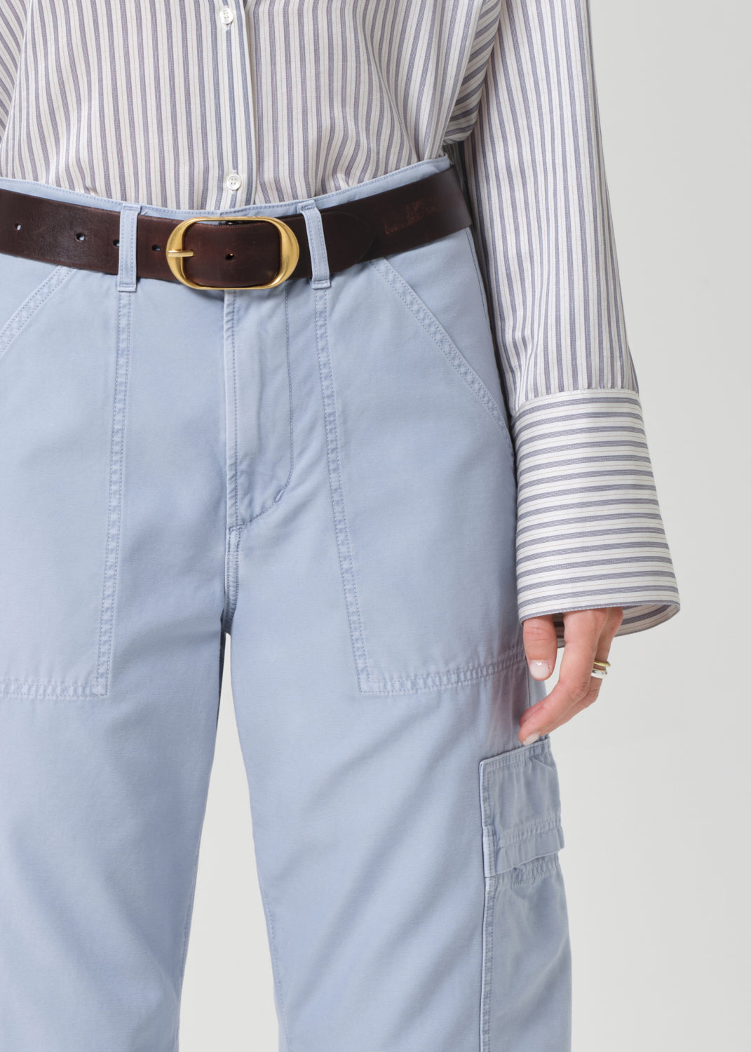 Person wearing a striped shirt and light blue cargo pants on a grey background
