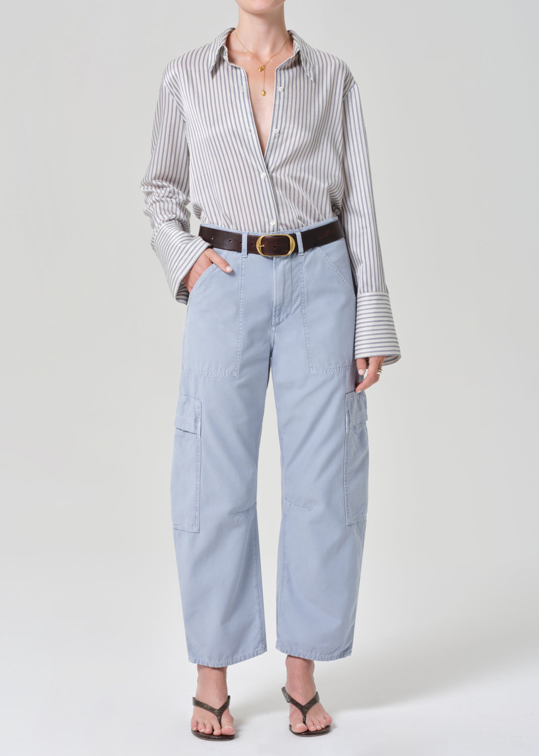 Person wearing a striped shirt and light blue cargo pants on a grey background