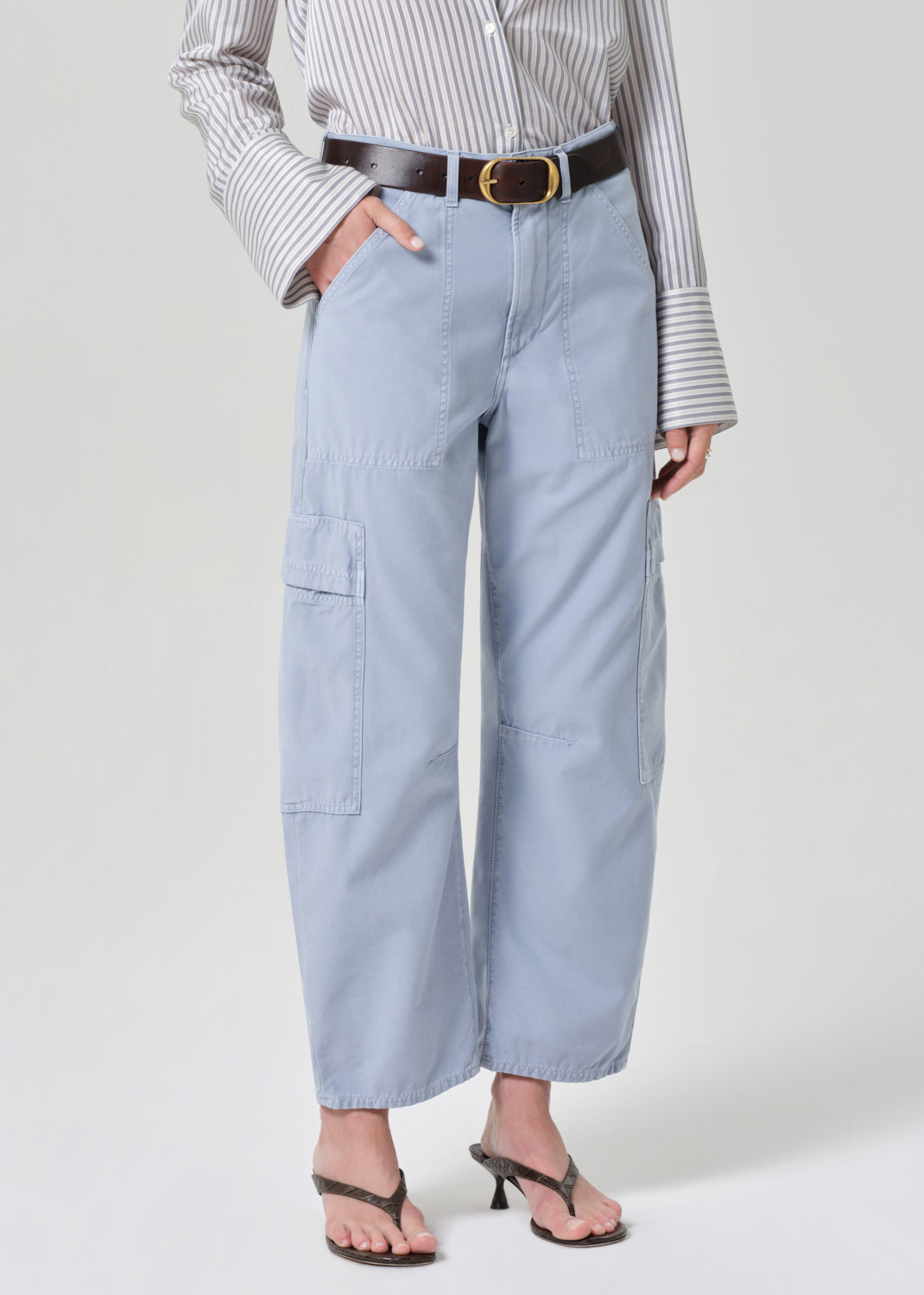Person wearing a striped shirt and light blue cargo pants on a grey background
