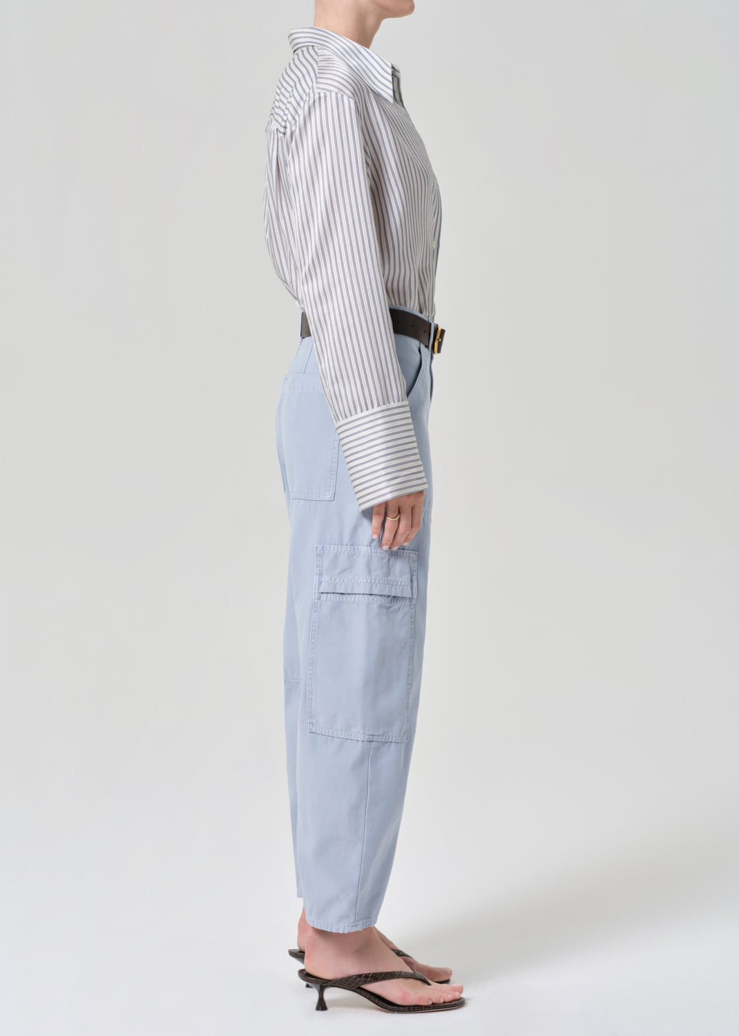 Person wearing a striped shirt and light blue cargo pants on a grey background