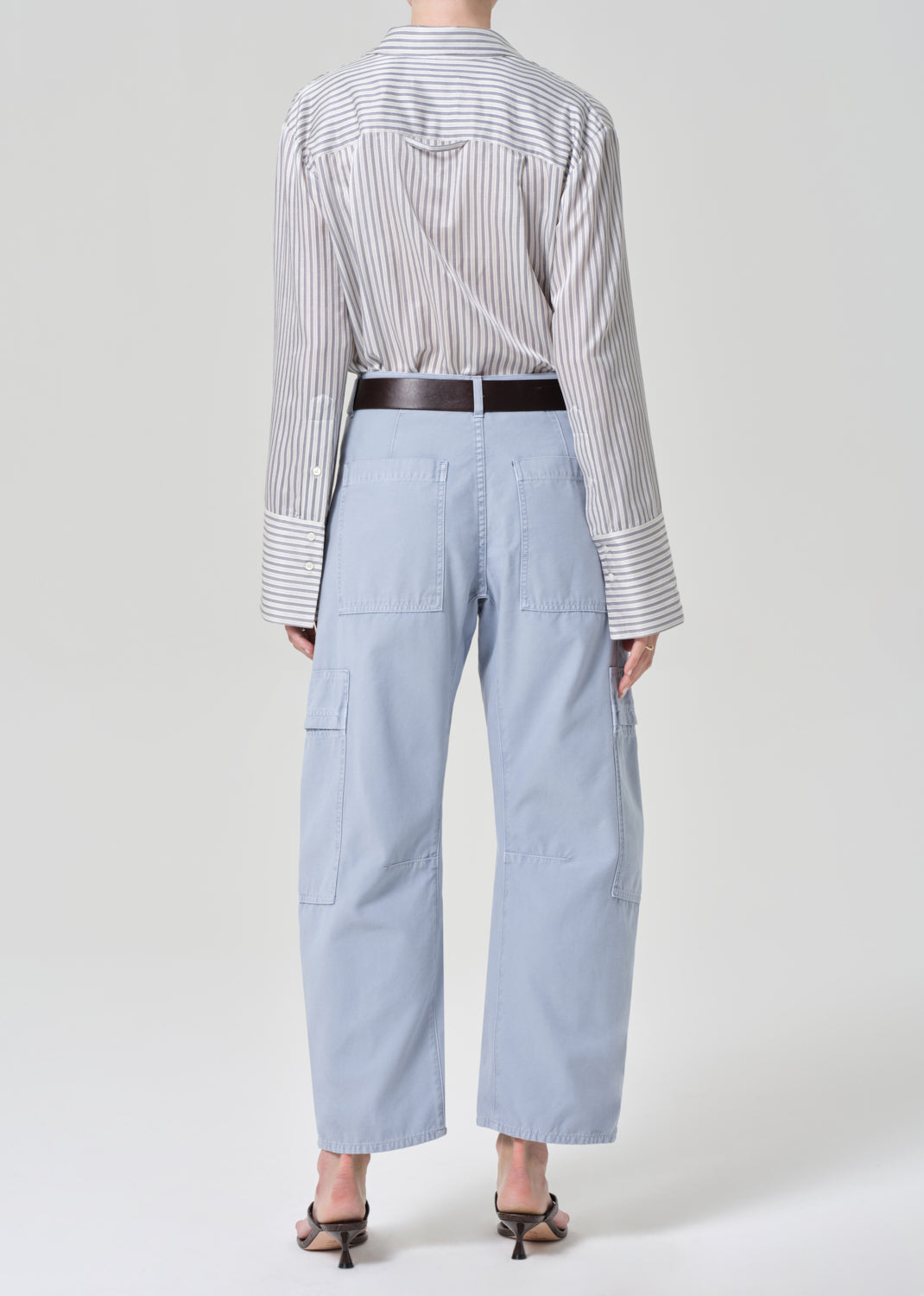 Person wearing a striped shirt and light blue cargo pants on a grey background
