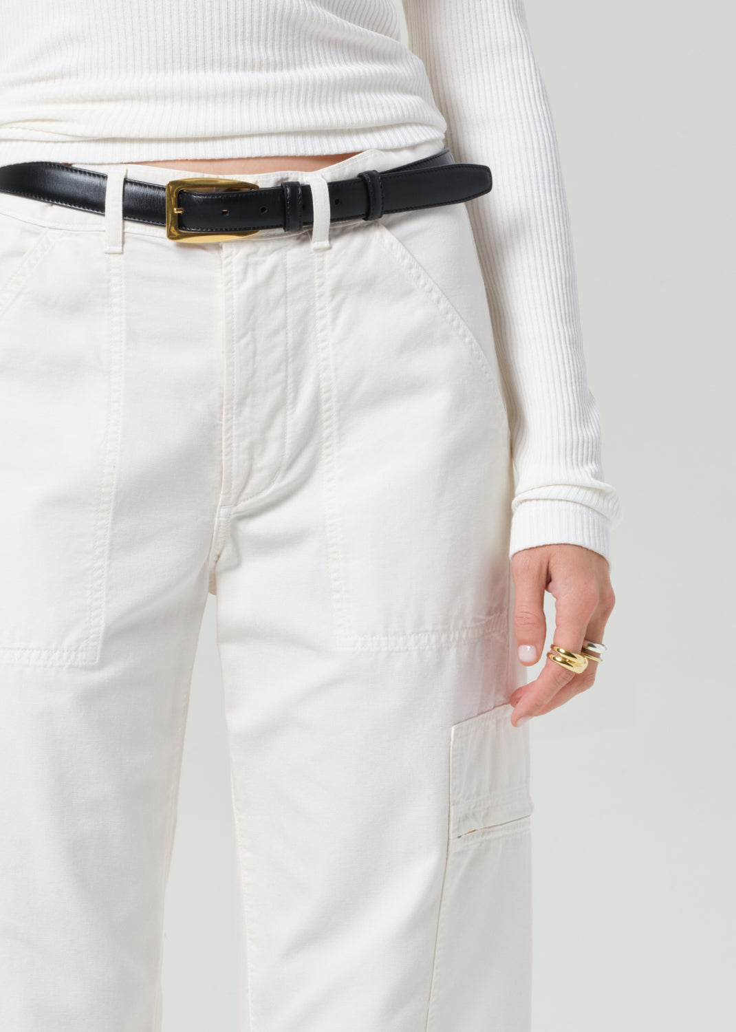 Person wearing a white long-sleeve top and light-colored pants with a black belt.