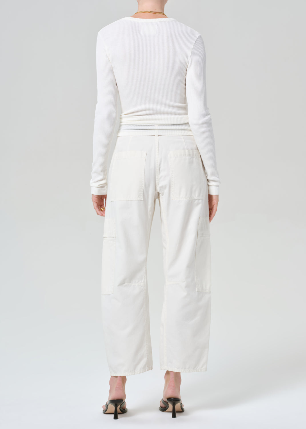 Person wearing a white long-sleeve top and wide-leg pants on a plain background