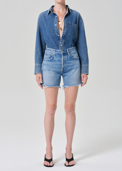 Person wearing a denim shirt and shorts on a grey background