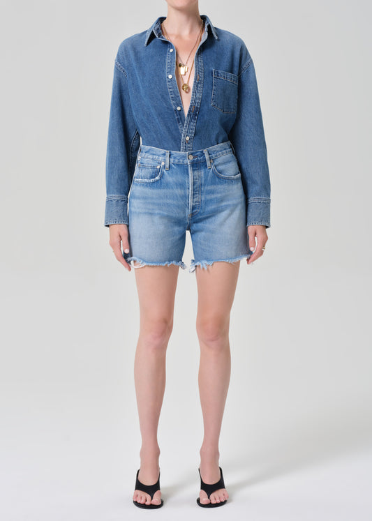 Person wearing a denim shirt and shorts on a grey background