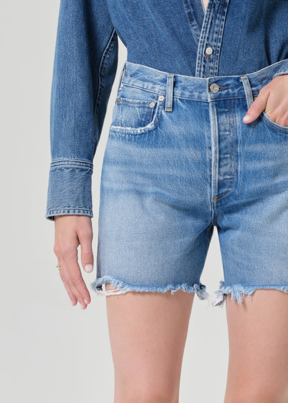 Person wearing a blue denim shirt and shorts on a plain background