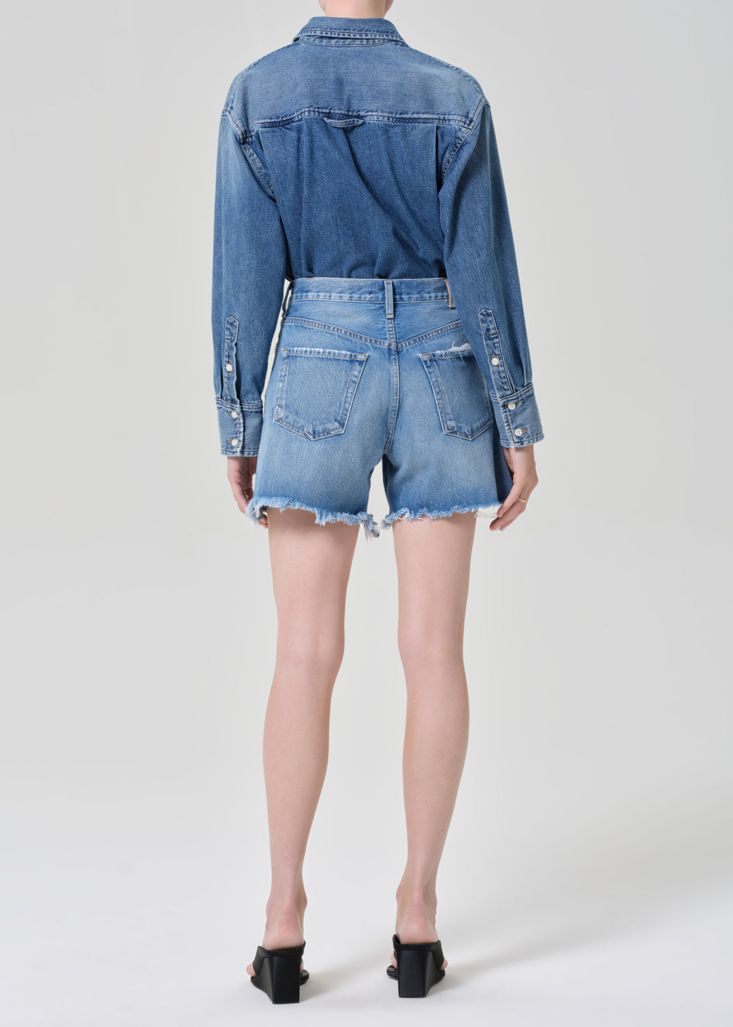Person wearing a denim shirt and shorts on a grey background