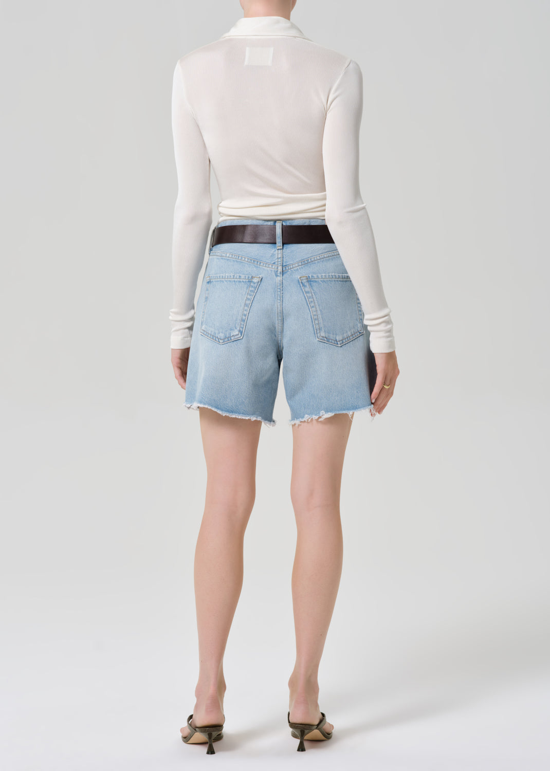 Person wearing light blue denim shorts and a white long-sleeve top on a white background