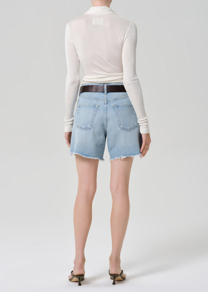 Person wearing light blue denim shorts and a white long-sleeve top on a white background