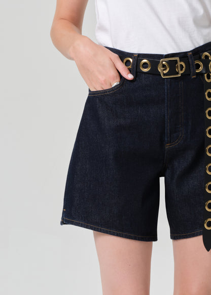 Person wearing black shorts with gold buttons on a grey background