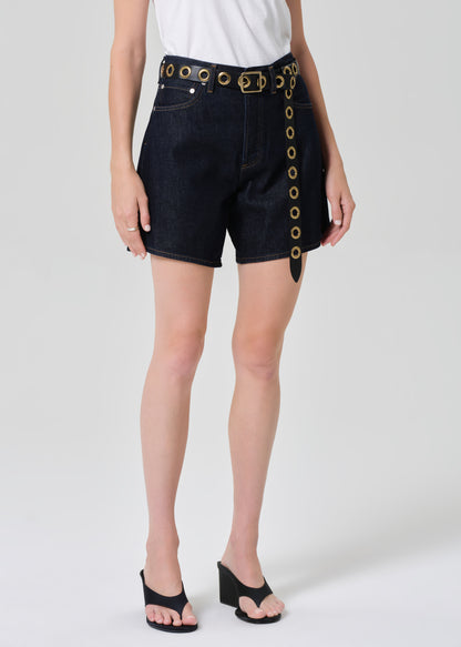 Person wearing black shorts with gold buttons on a grey background