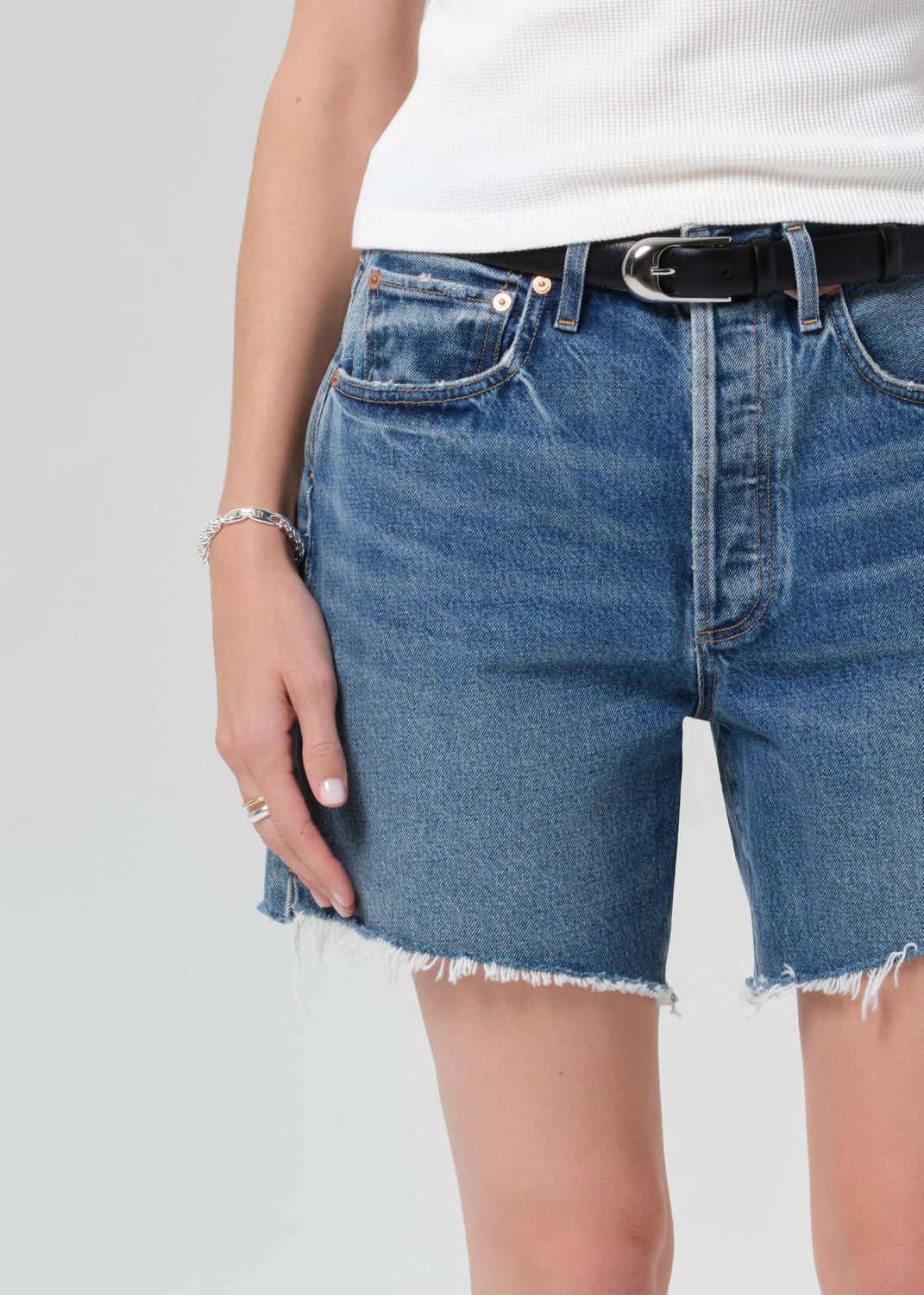 Person wearing a white top and blue denim shorts on a plain background