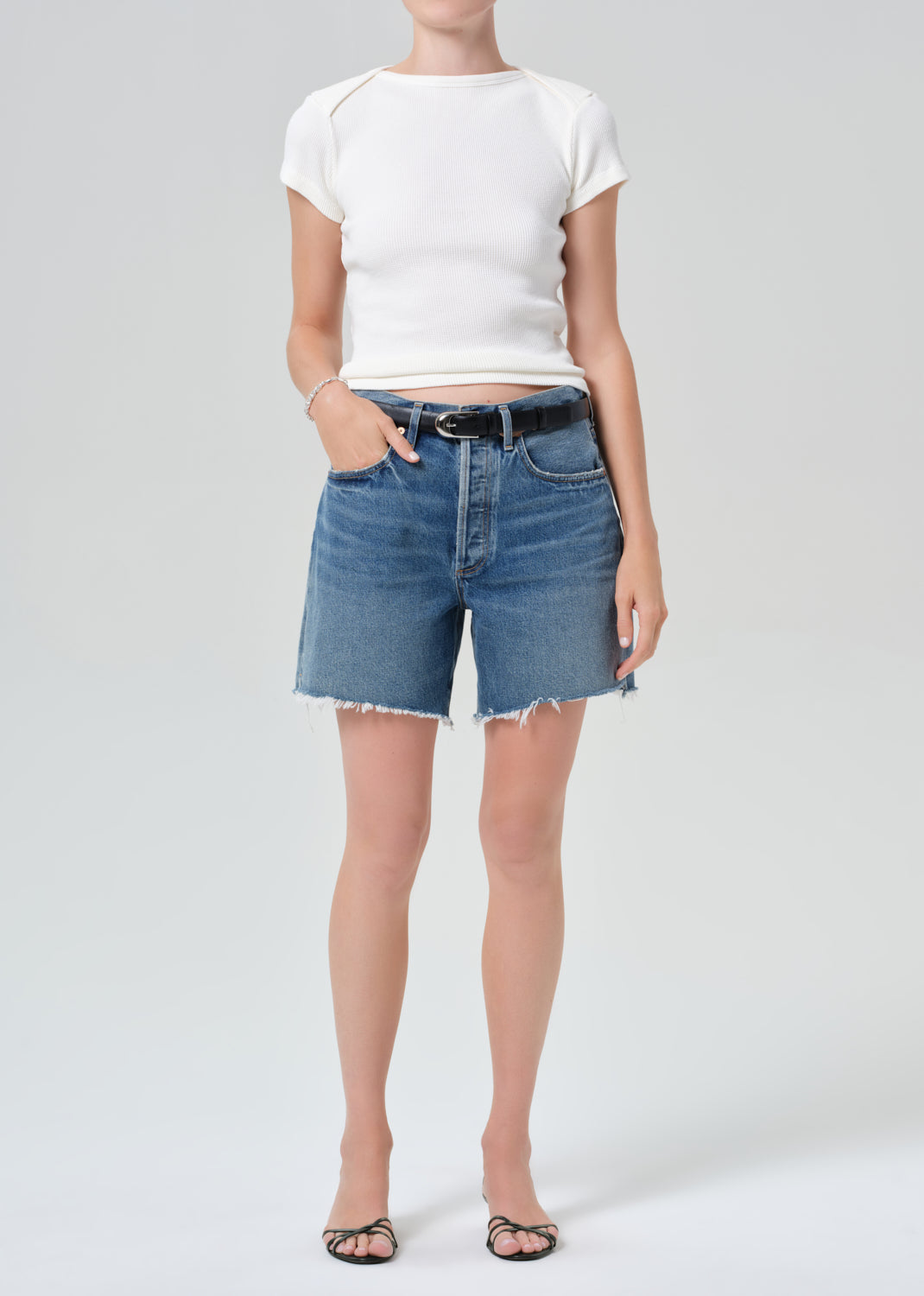 Person wearing a white top and blue denim shorts on a plain background
