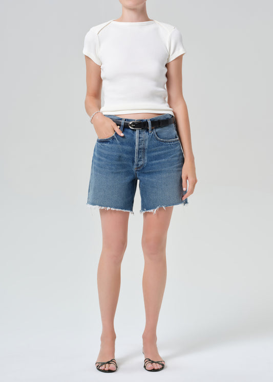 Person wearing a white top and blue denim shorts on a plain background