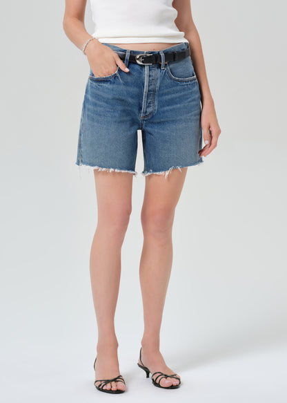 Person wearing a white top and blue denim shorts on a plain background