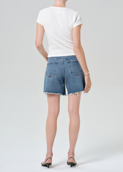 Person wearing a white top and blue denim shorts on a plain background