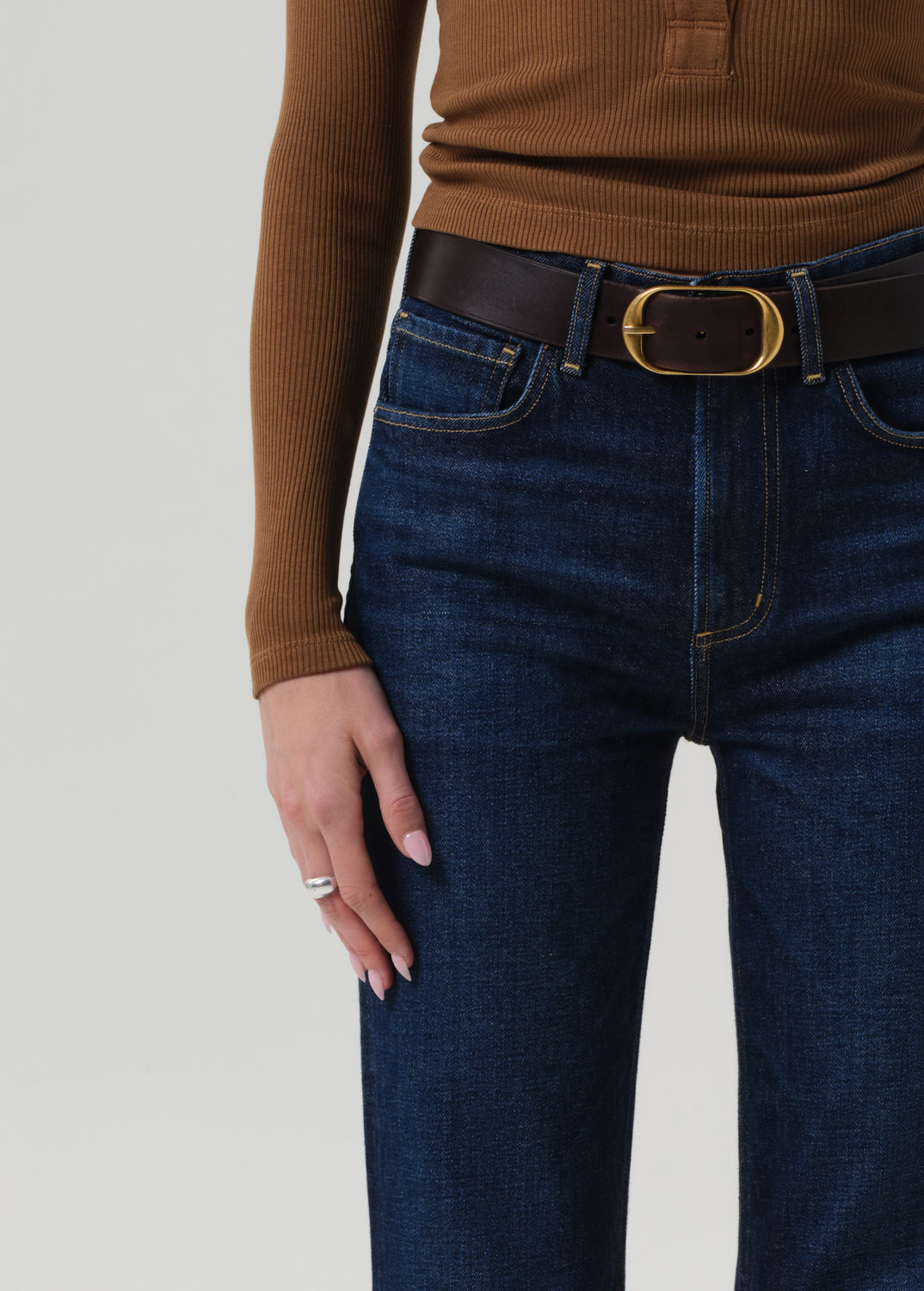 Person wearing a brown ribbed sweater and blue jeans with a belt on a light gray background
