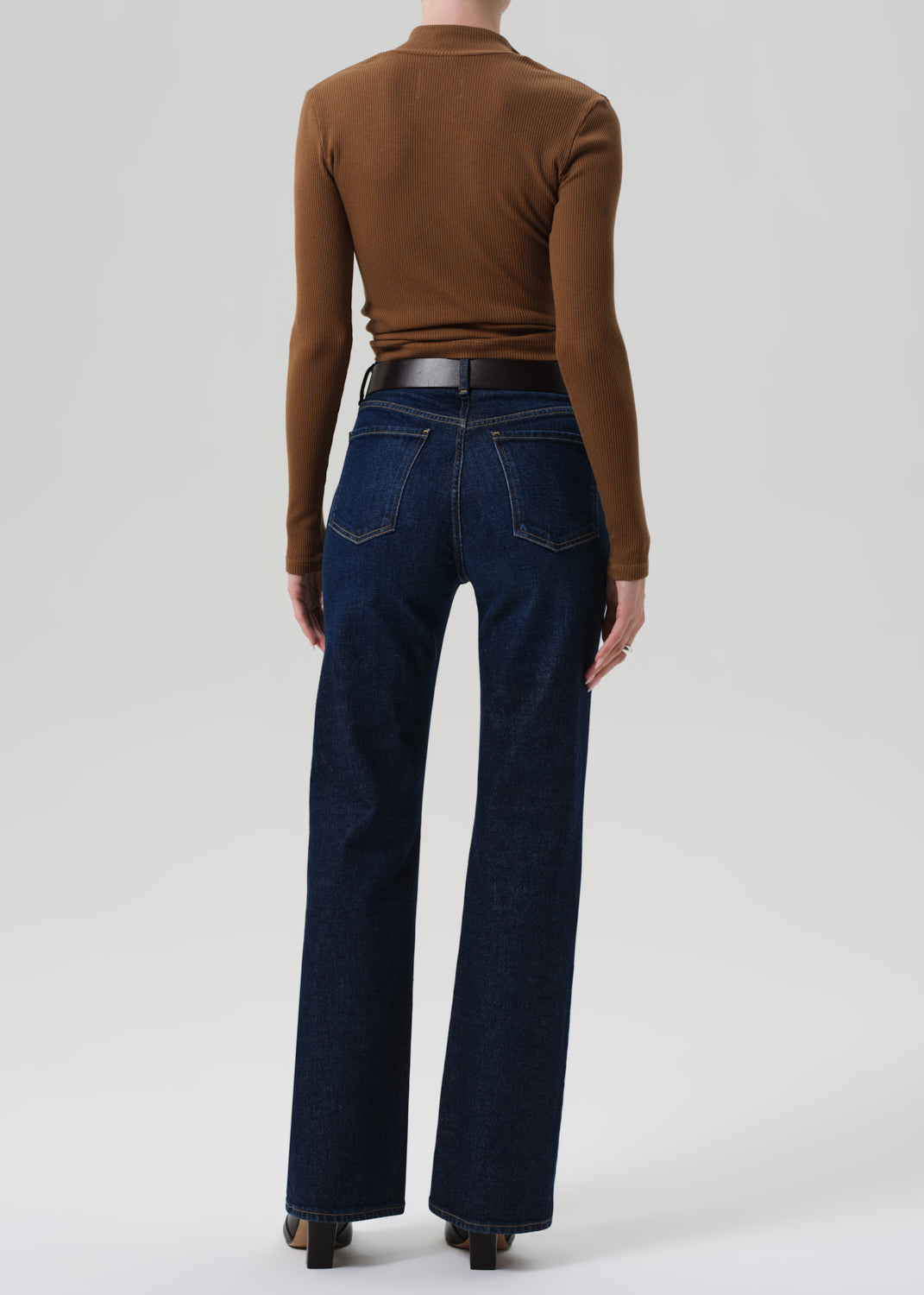 Person wearing a brown long-sleeve top and dark blue jeans on a white background