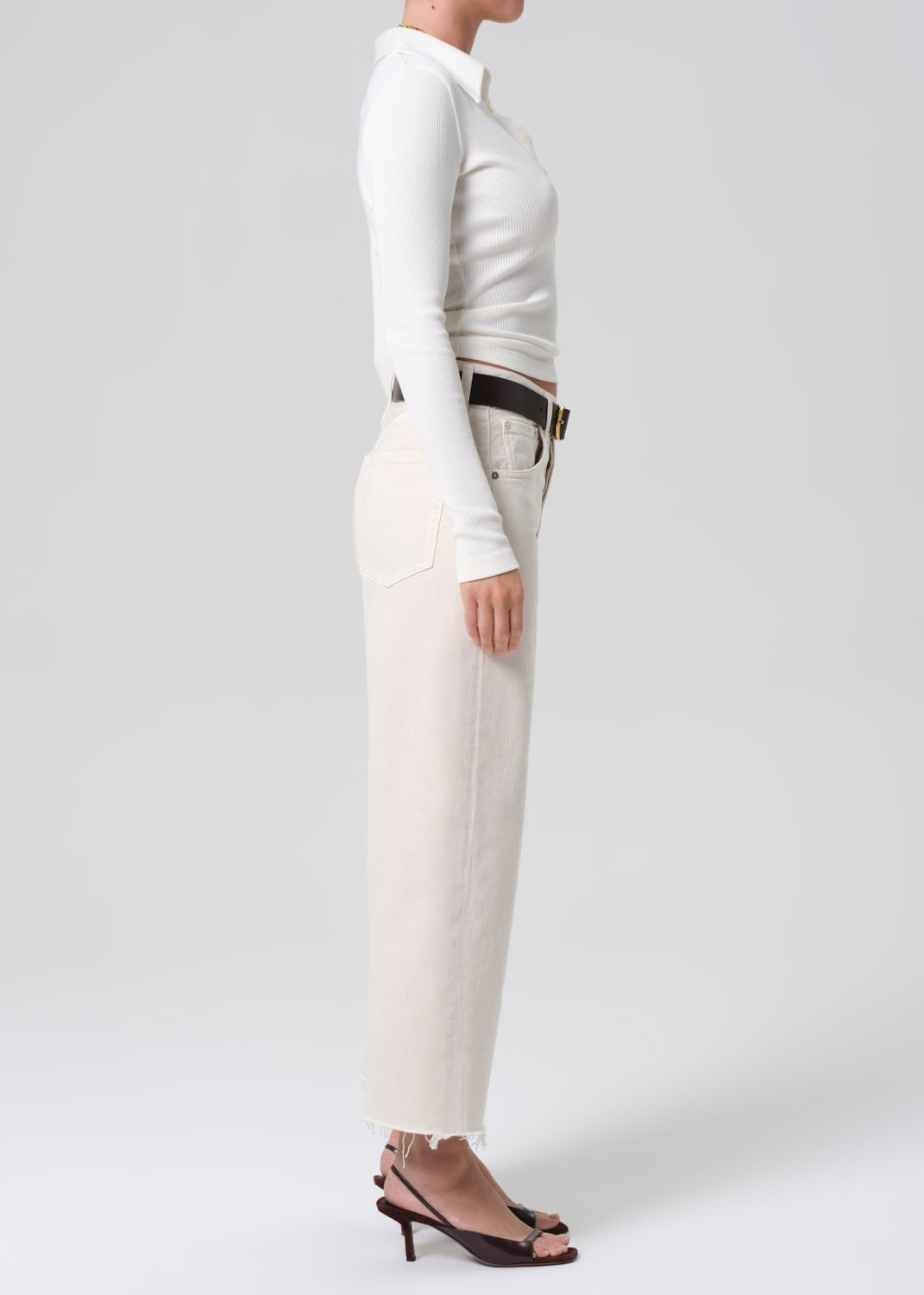 Person wearing a white long-sleeve top and beige pants on a plain background