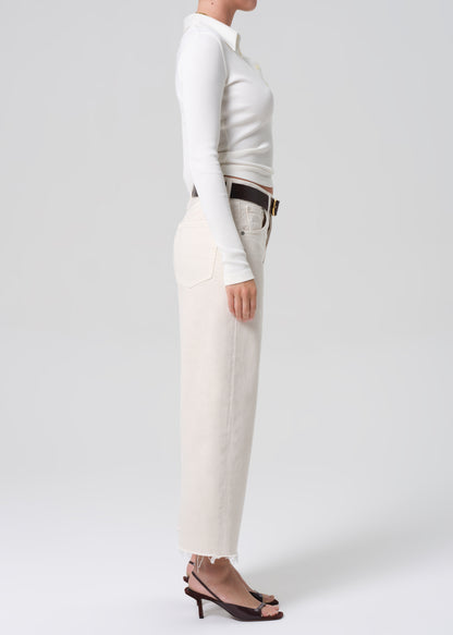 Person wearing a white long-sleeve top and beige pants on a plain background