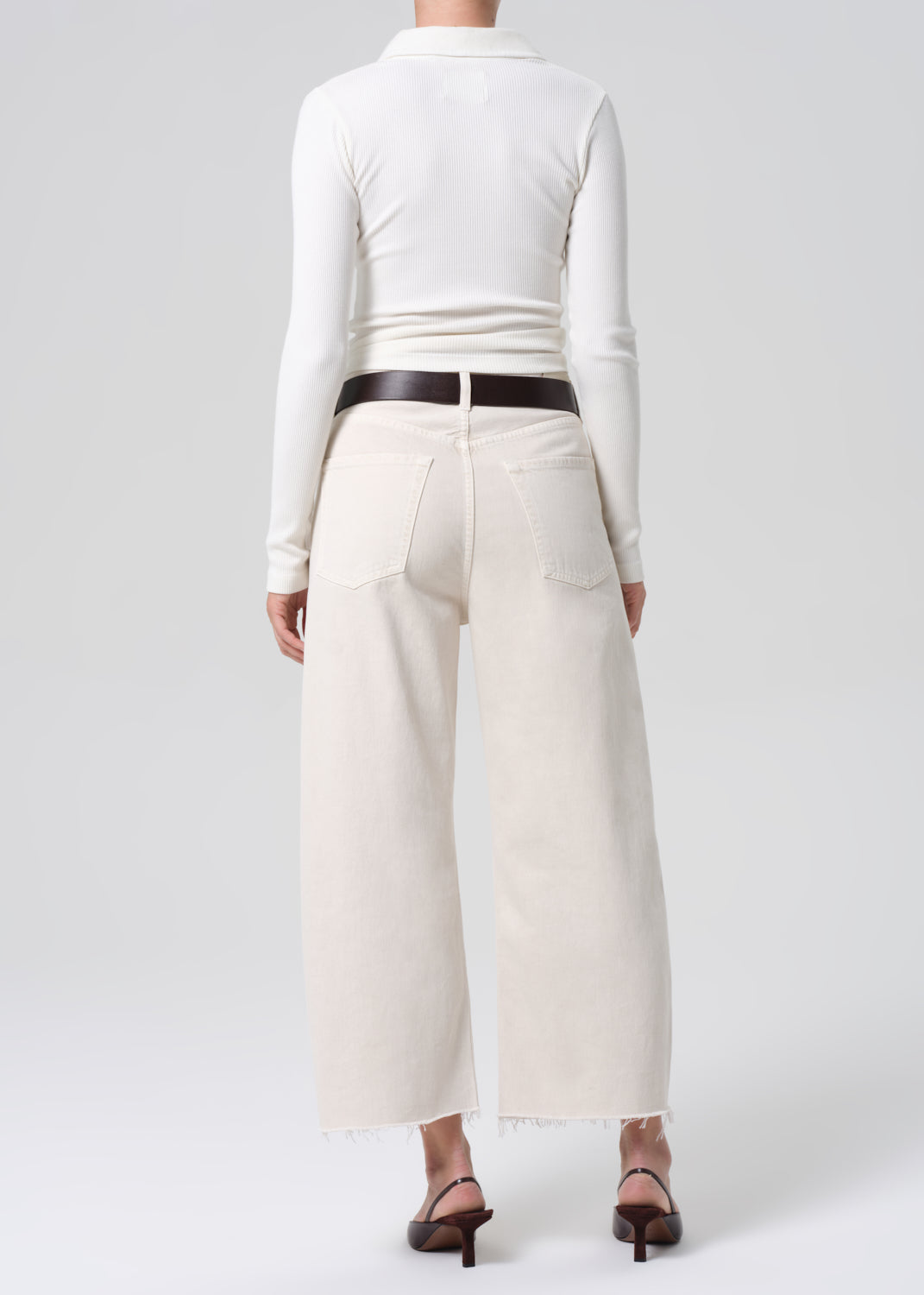 Person wearing a white long-sleeve top and cream-colored wide-leg pants on a white background