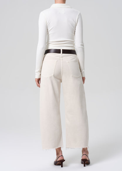 Person wearing a white long-sleeve top and cream-colored wide-leg pants on a white background
