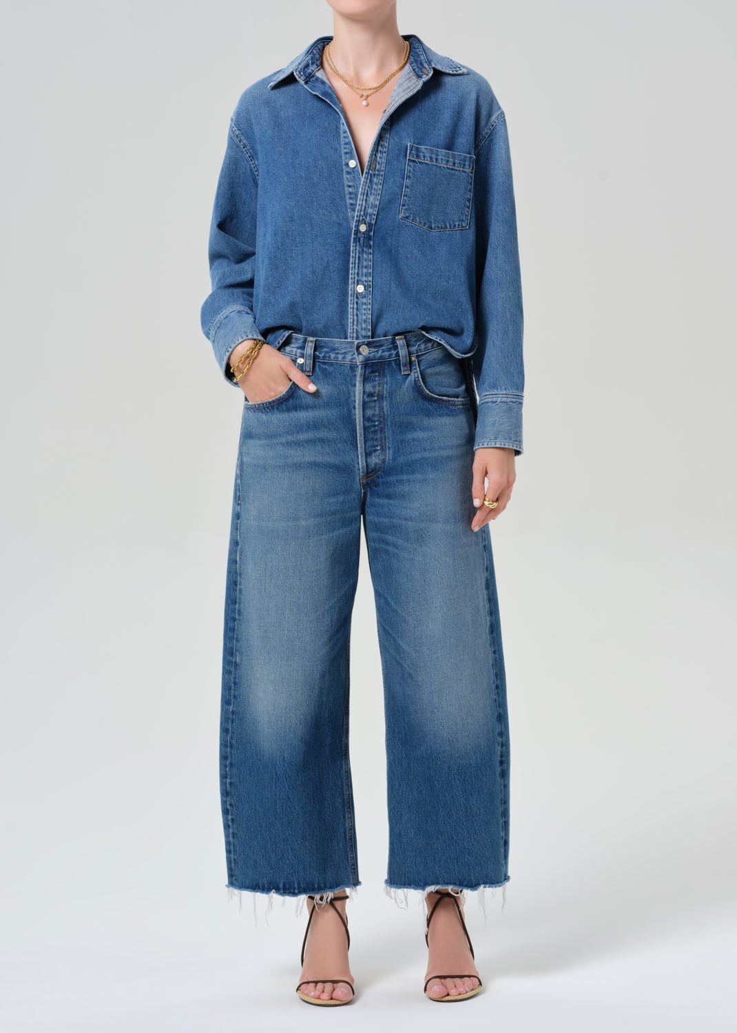 Person wearing a denim shirt with cropped jeans on a grey background