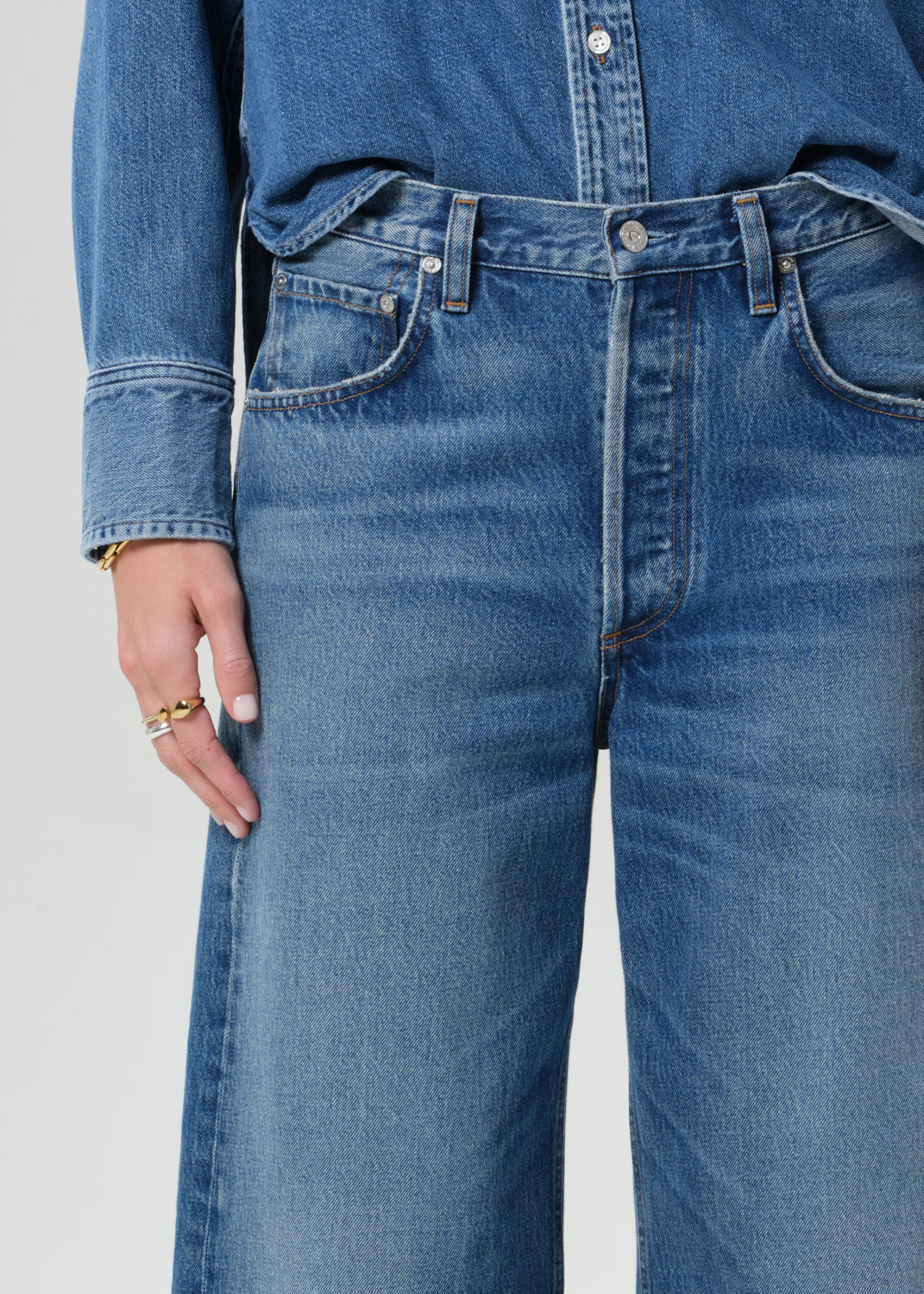 Person wearing a denim shirt with cropped jeans on a grey background