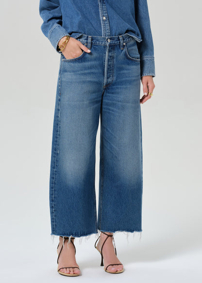 Person wearing a denim shirt with cropped jeans on a grey background