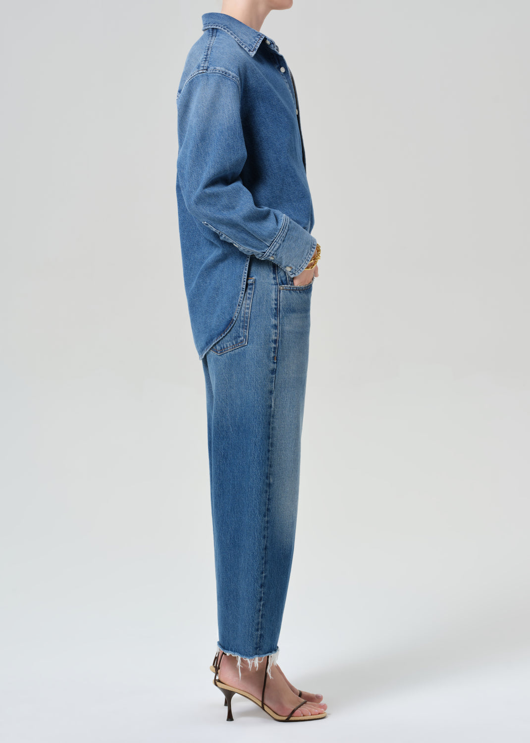 Person wearing a denim shirt with cropped jeans on a grey background